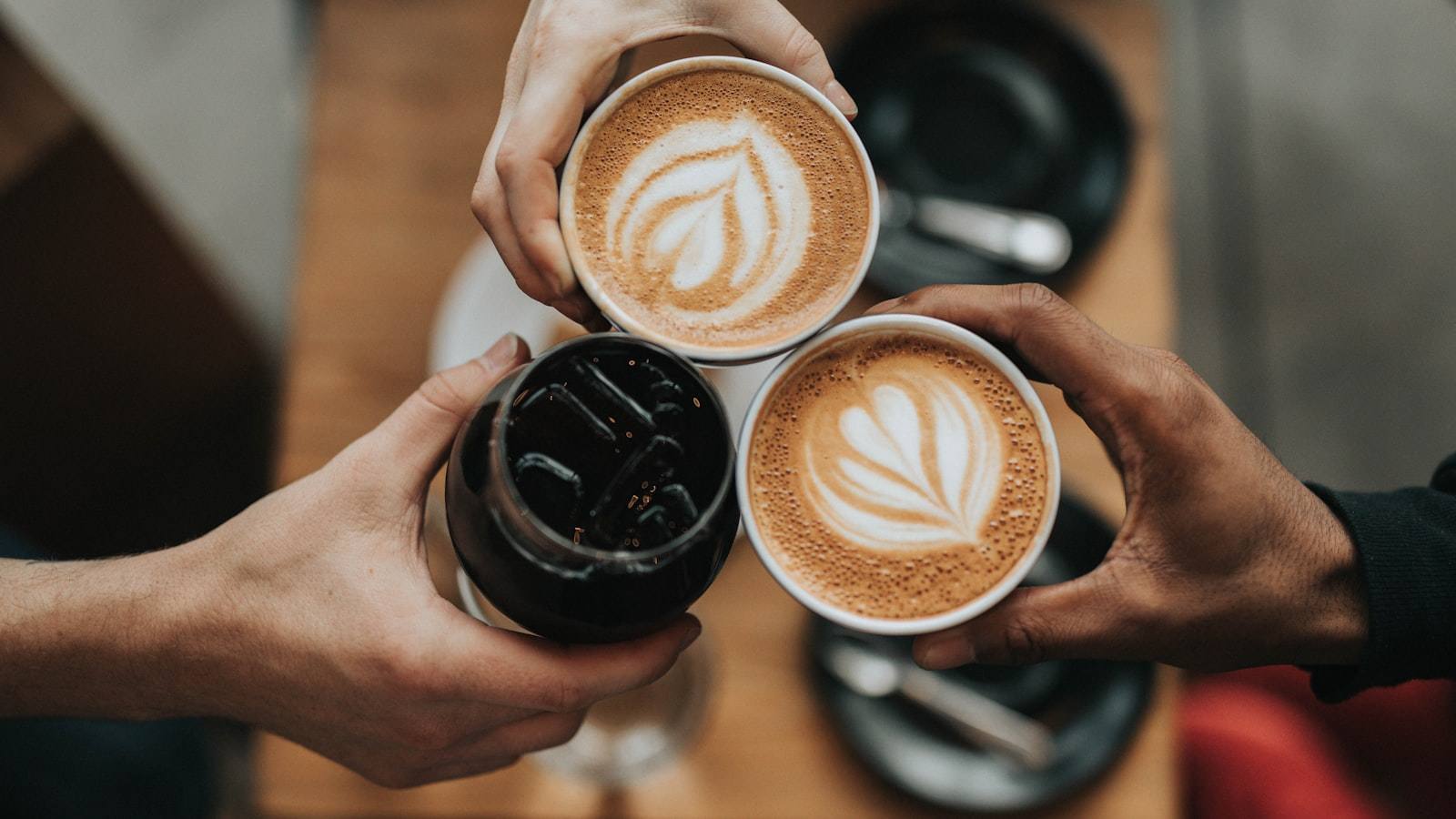 Coffee cups on a wooden cafe table, hands gathering for a toast